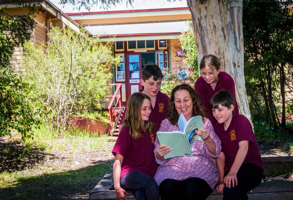 Chewton Primary School principal Bernadette McKenna flicks through the 150-year history of the school with current students (from left) Frederica Amati, Archie Culph (second generation of family at the school), Amelia Birdsall and Aiden Mawson (fourth generation of family at the school). Picture by Brendan McCarthy