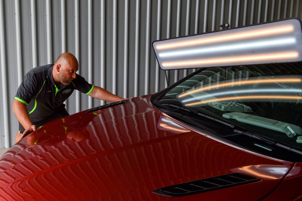 Jesse Bryan from Bendigo Denton Solutions assesses the hail-pocked bonnet of a car damaged in the January 2 storm. Picture by Darren Howe