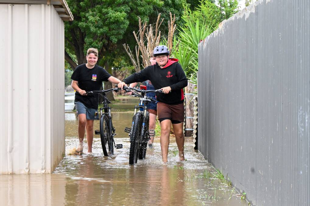 Tom, Ryder and Cooper push their bikes on a flooded section of the Midland Highway at Huntly on Monday early afternoon.
