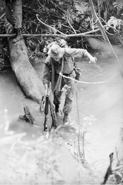 A signaller of 9RAR balances precariously on a log during a river crossing. Picture courtesy of Christopher John Bellis/Australian War Memorial