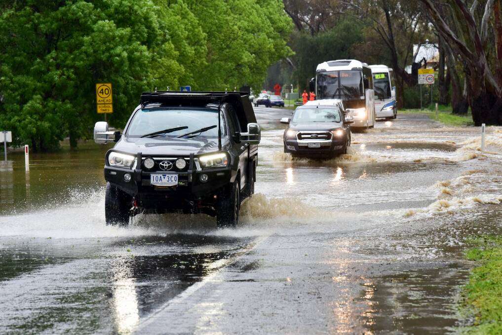 Vehicles negotiate floodwaters on the Calder Highway under the watchful eye of emergency service workers, who would soon close the road. Picture by Brendan McCarthy.