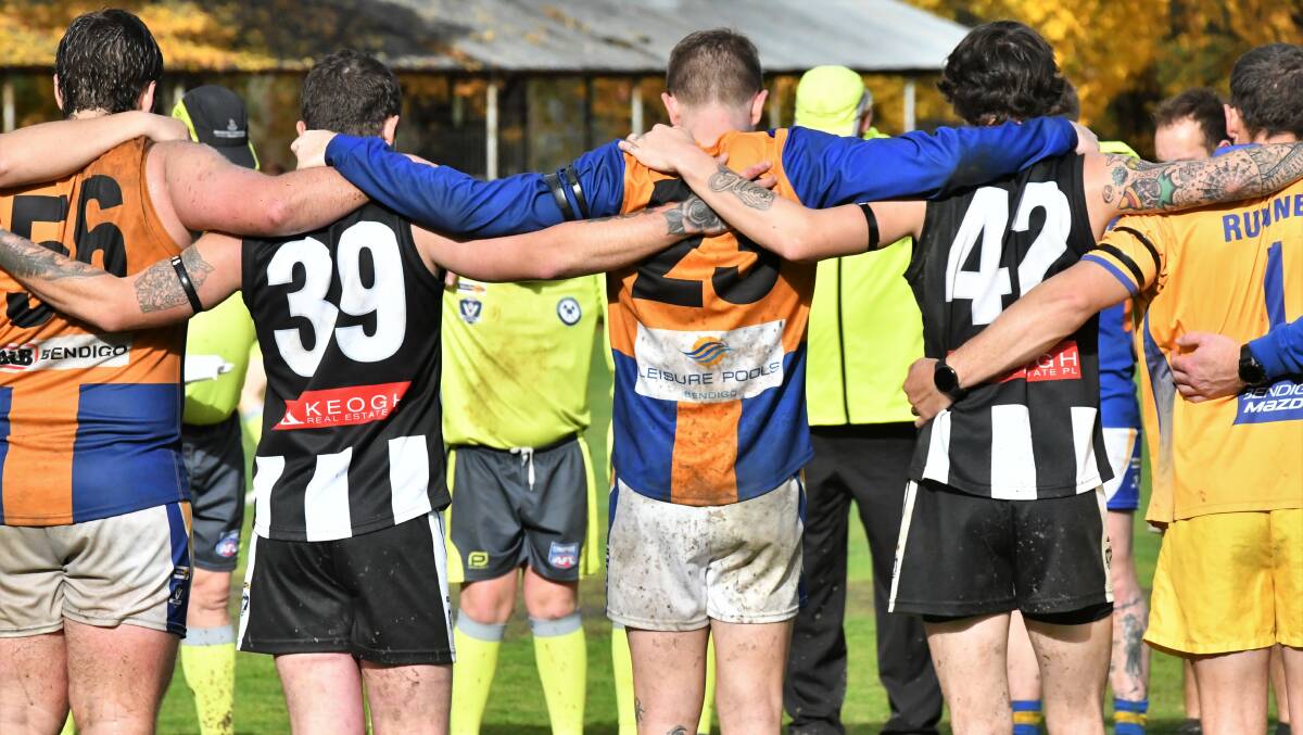 Castlemaine and Golden Square players embrace for one minute silence at the Camp Reserve. Picture by Adam Bourke